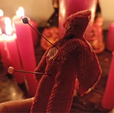Muñeco de tela rosada entre velas rosadas encendidas