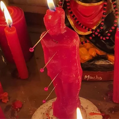 Figura de cera roja con alfileres junto a velas rojas